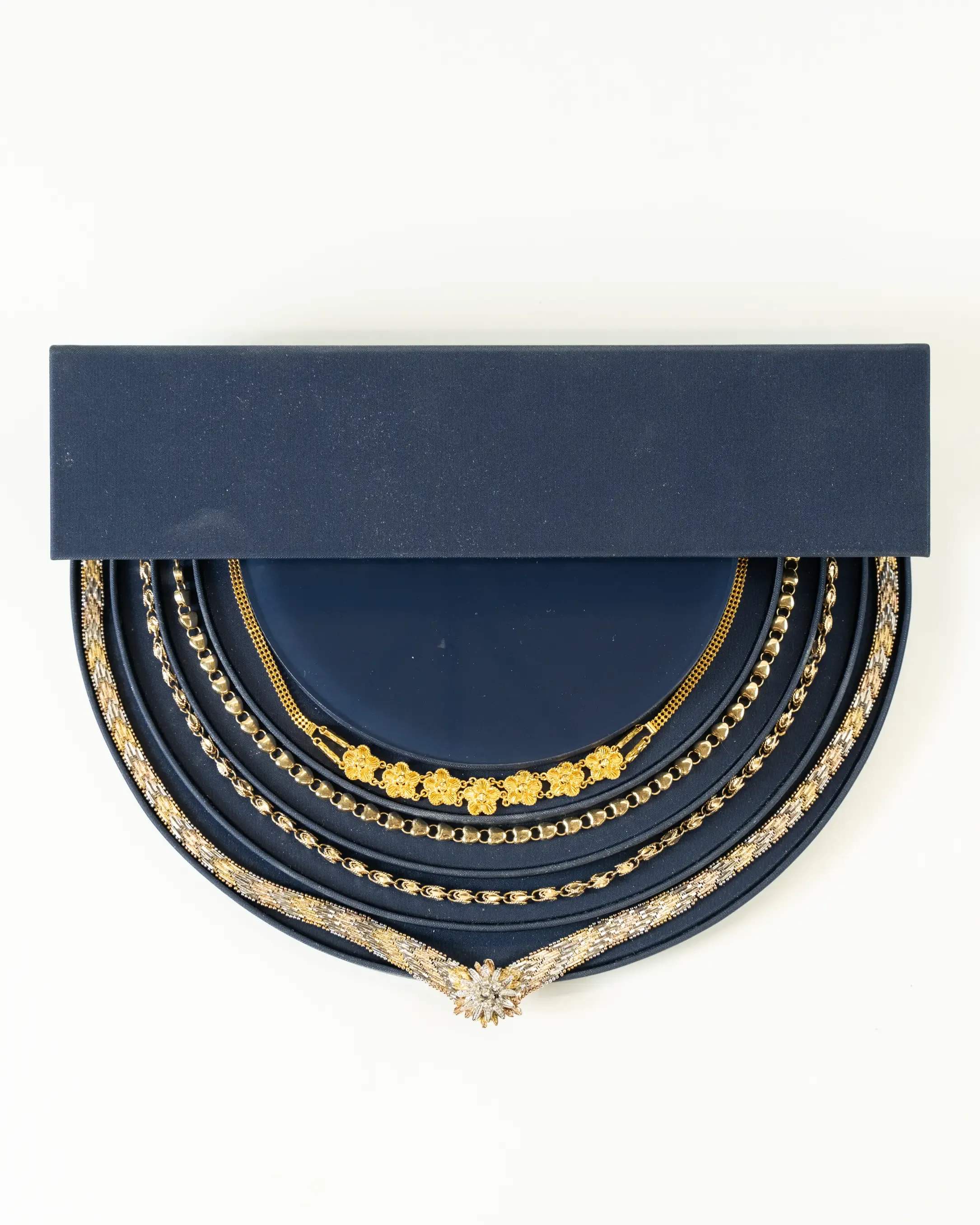 Set of elegant gold and silver necklaces with intricate designs displayed on a navy blue presentation board with a matching rectangular cover.