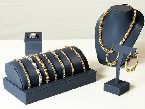 Elegant display of gold and silver jewelry including bracelets, a ring, hoop earrings, and a gold chain necklace on navy blue stands.