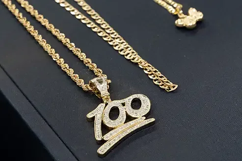 Close-up of gold necklaces displayed on a dark surface, featuring various chain styles and a standout pendant with a diamond-encrusted
