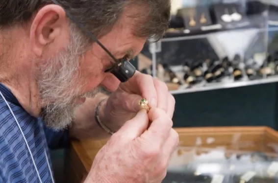 A man examining a ring with a magnifying glass, likely appraising jewelry.
